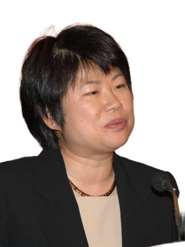 Woman with short black hair at a podium in front of a colorful banner