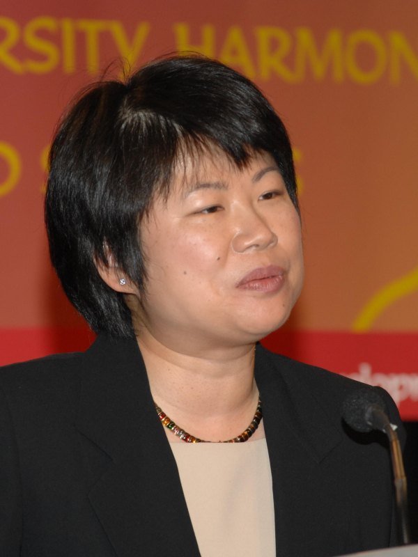 Woman with short black hair at a podium in front of a colorful banner